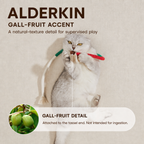 Cat holding a flexible rope toy with tassels and a gall-fruit accent